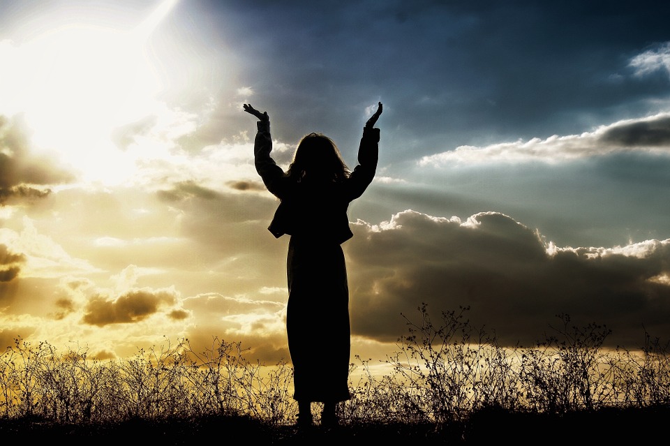 Lady standing in a field and raising arms to the skies