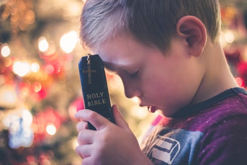 Little boy holding a Bible while praying