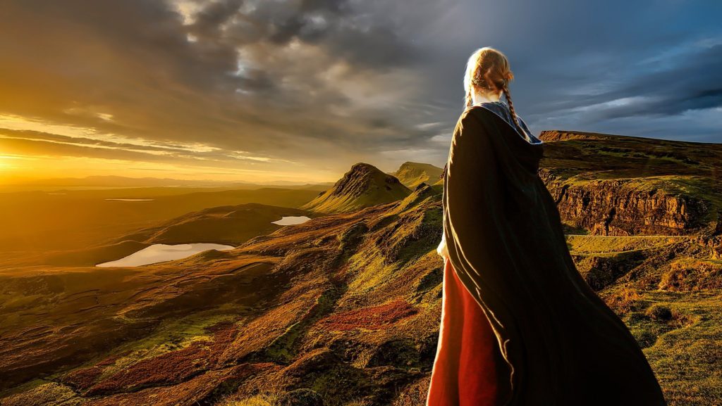 Lady wearing black cape staring at a mountain range